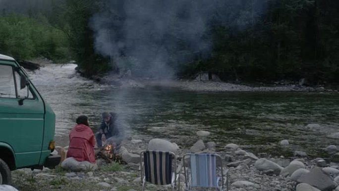 年轻夫妇在炉火旁放松。露营者在后台。山地景观