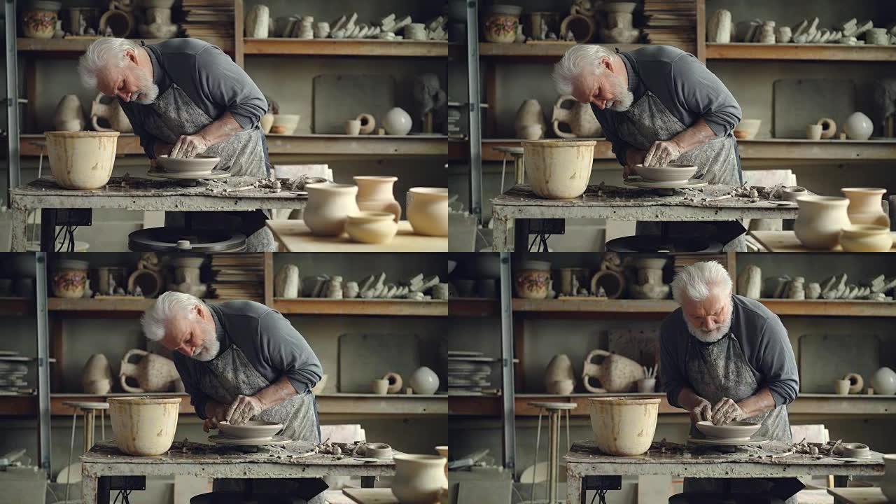 经验丰富的高级大师正在小作坊的陶轮上制作低粘土碗。可以看到陶瓷夹具，手工制作的粘土器皿和陶工工具。