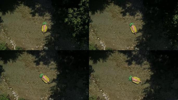 空中慢动作: 年轻的女性在菠萝漂浮物上晒黑，在河上滑行。