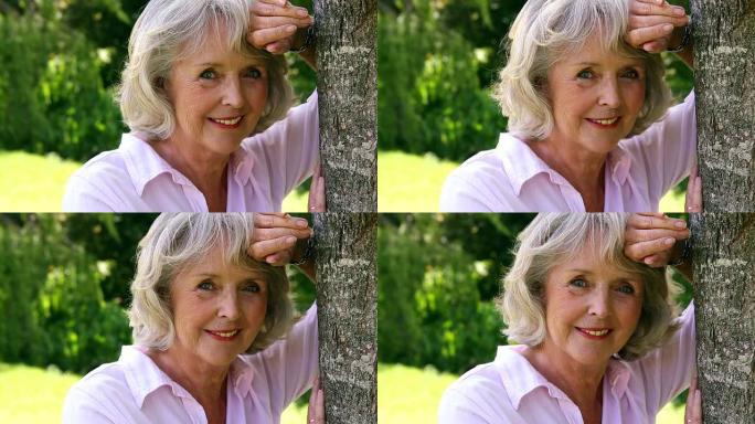 退休妇女靠在树上，对着镜头微笑