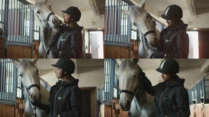 年轻的骑师女孩正在马stable里抚摸一匹白马。