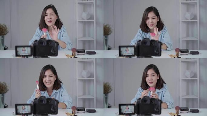 快乐微笑的亚洲女人或美容博主用刷子和相机录制视频，并在家里挥手。美女视频博客博客人物概念。