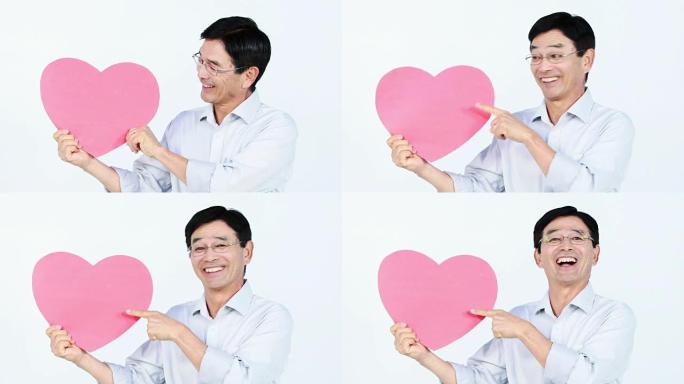微笑的亚洲男子抱着一颗粉红色的心