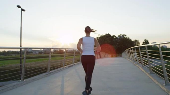 慢动作: 活跃的女孩在城市的桥上奔跑，进入神奇的夕阳