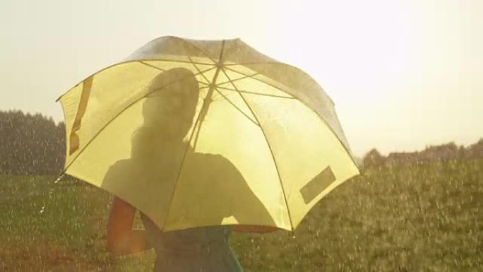 太阳耀斑: 快乐的女人在春雨中旋转，同时拿着黄色的雨伞