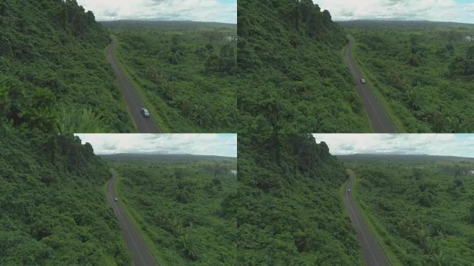空中: 白色汽车沿着空旷的柏油路行驶，周围是茂密的雨林。