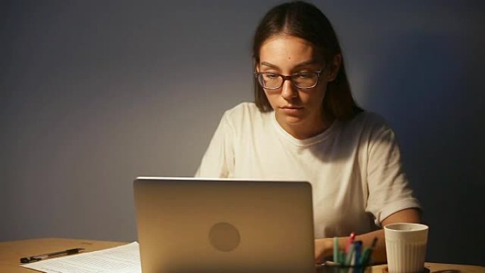 年轻的休闲女性在带文件的pc笔记本电脑上工作到很晚