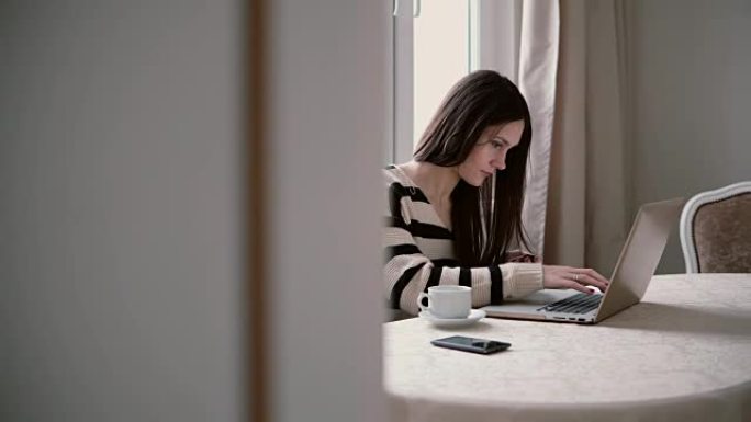 女人使用笔记本电脑，在明亮的用餐中享受早晨的咖啡。向右滑动，通过打开的门查看