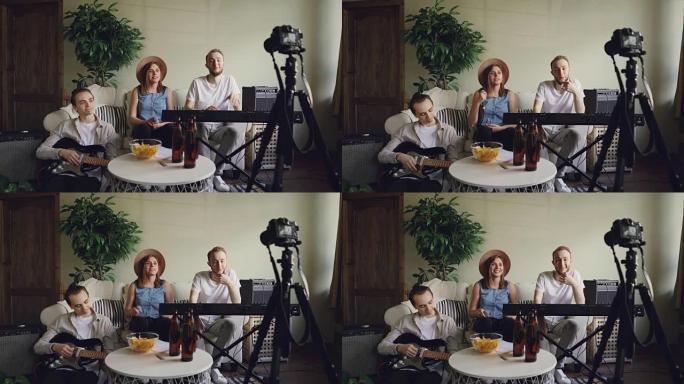 流行乐队的年轻成员正在用相机录制在线博客的视频。迷人的女歌手拿着麦克风说话，她的朋友们在微笑。