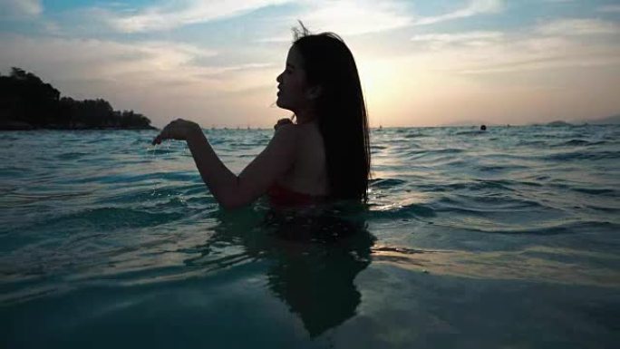 穿着比基尼的亚洲性感女孩，头发和嘴唇湿湿，在海上的日落中嬉戏