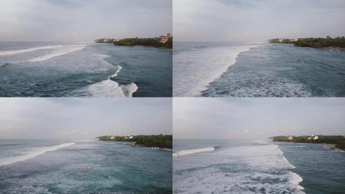 空中无人机拍摄了令人惊叹的泡沫海浪在热带度假胜地海岸到达并破裂的酒店和房屋
