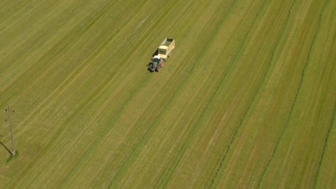 空中: 农民在拖拉机上，拖车在农田上捡拾干草