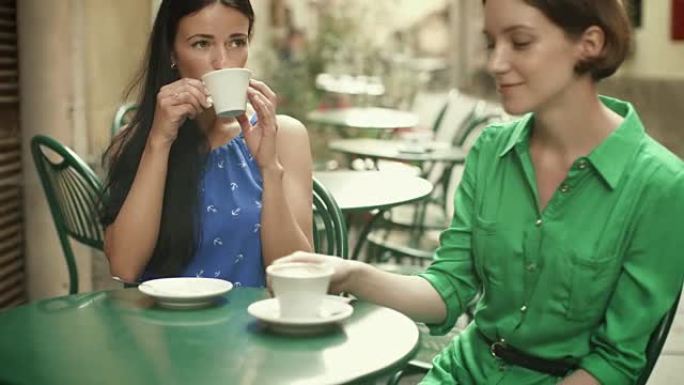 两个穿着浅色夏装的迷人年轻女性在街头咖啡店放松和交谈。