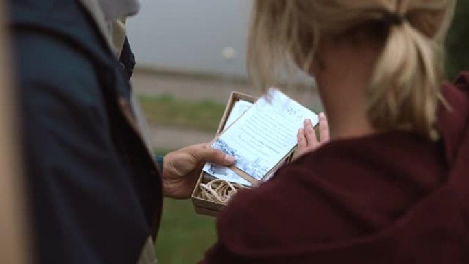 年轻夫妇打开明信片上有礼物和阅读问候的盒子的特写视图。男人和女人的浪漫约会