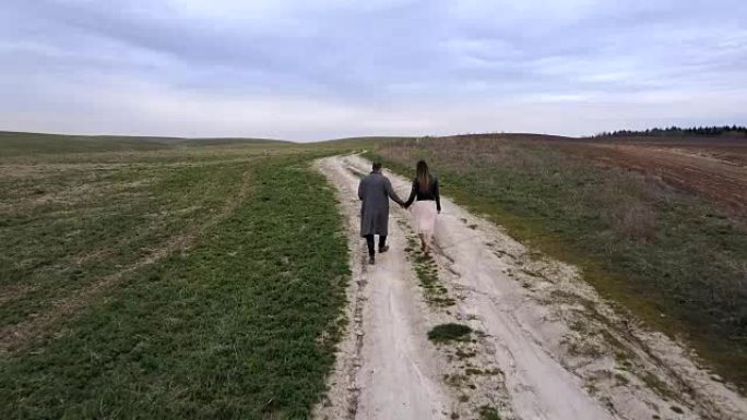 年轻的男人和女人穿过乡村。鸟瞰图，无人机飞过一对在球场上行走的夫妇。后视图