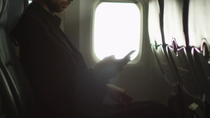 年轻人正在窗户旁边的飞机内使用智能手机。