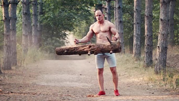 光着膀子的健美运动员在森林路上用原木做卷发