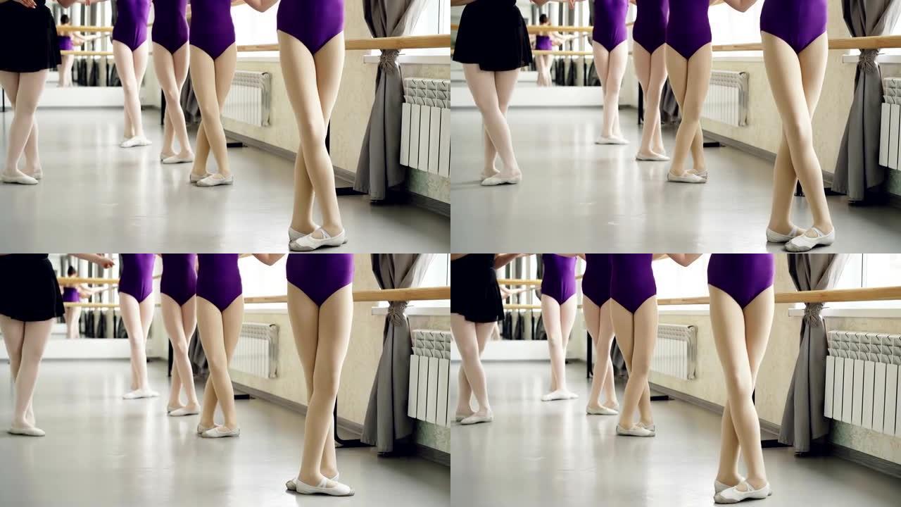 穿着紧身衣的苗条女孩的腿在芭蕾舞课上与经验丰富的女老师一起做tedu，演示动作并检查学生。