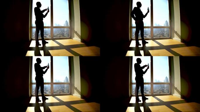 男人在大窗户上打开百叶窗的轮廓。阳光照进房间，产生阴影。