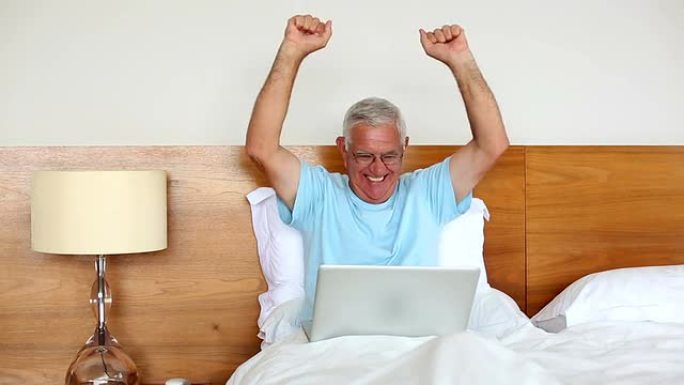 坐在床上的老人用笔记本电脑欢呼