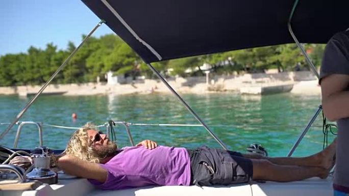 4k男子放松，躺在阳光明媚的帆船上，实时