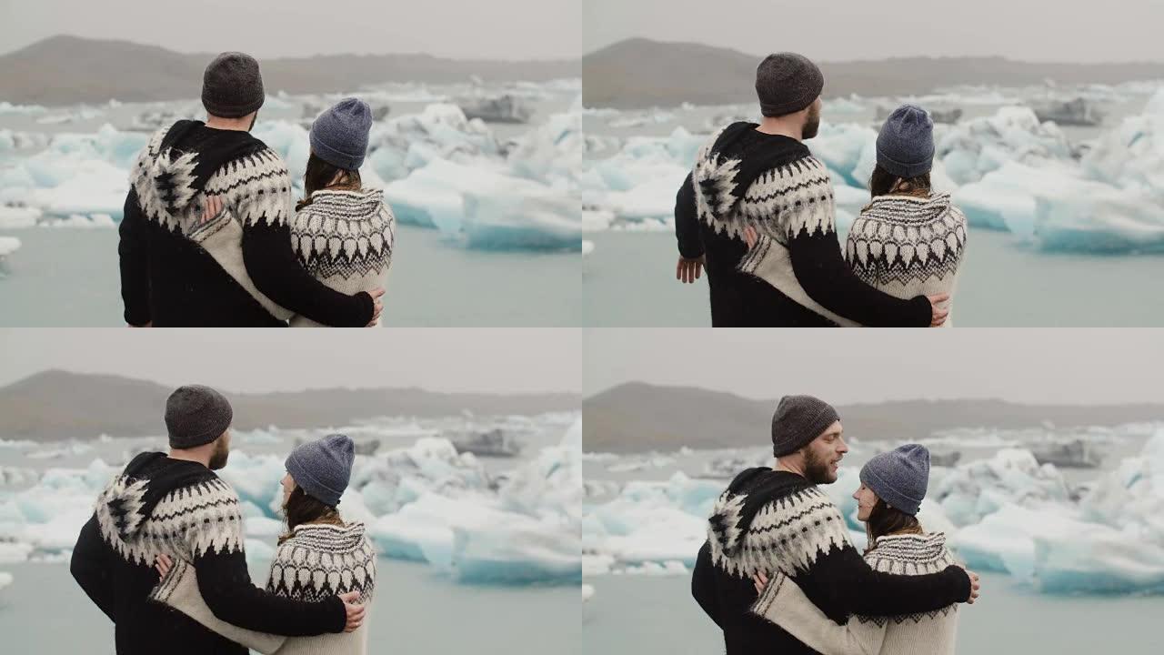 站在冰泻湖的年轻夫妇的后视图。男人亲吻女人并拥抱她，看着冰岛的冰川