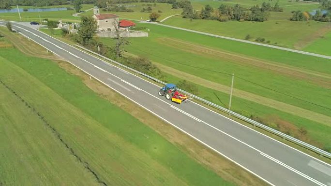 空中: 拖拉机沿着空旷的乡村道路驶过郁郁葱葱的绿色田野