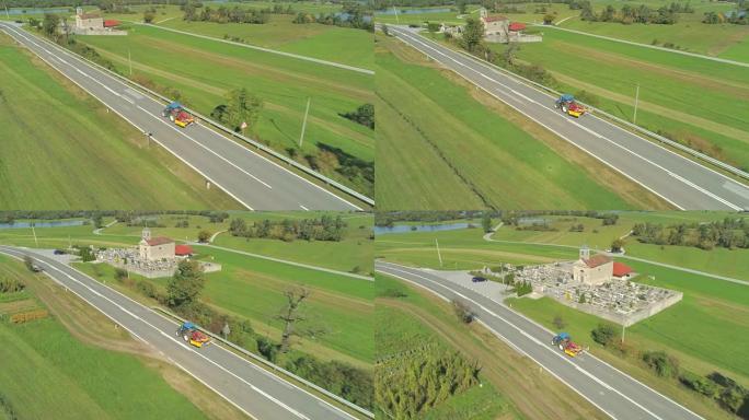 空中: 拖拉机沿着空旷的乡村道路驶过郁郁葱葱的绿色田野