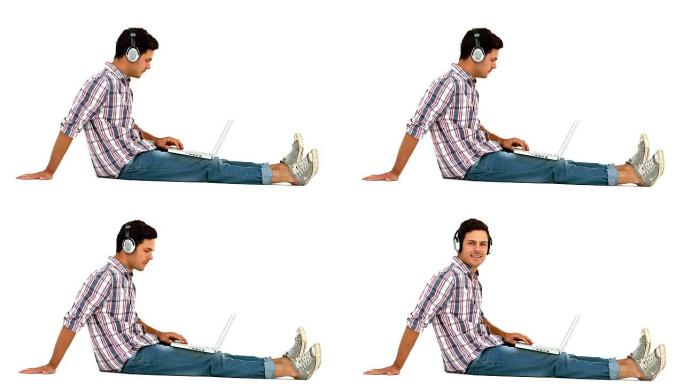 戴着耳机的男人坐在地板上使用笔记本电脑