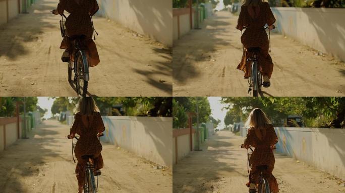 一个穿着连衣裙的美女骑着自行车穿过小镇的狭窄街道。南亚自然，棕榈树生长在路边。慢动作。