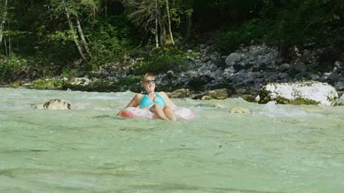 慢动作年轻女孩在甜甜圈漂浮物上滑翔在河水中飞溅
