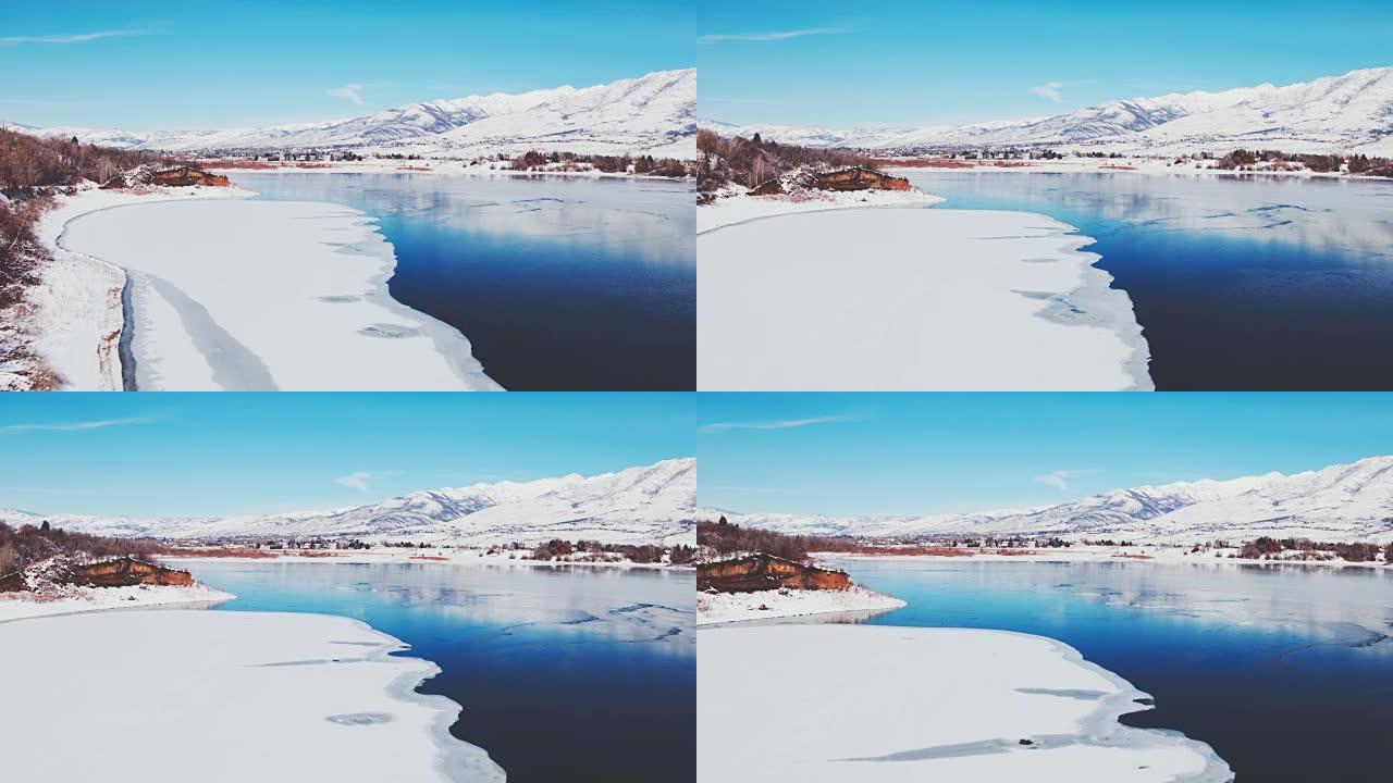 鸟瞰图飞越冬季湖，冰雪覆盖，背景为雪山