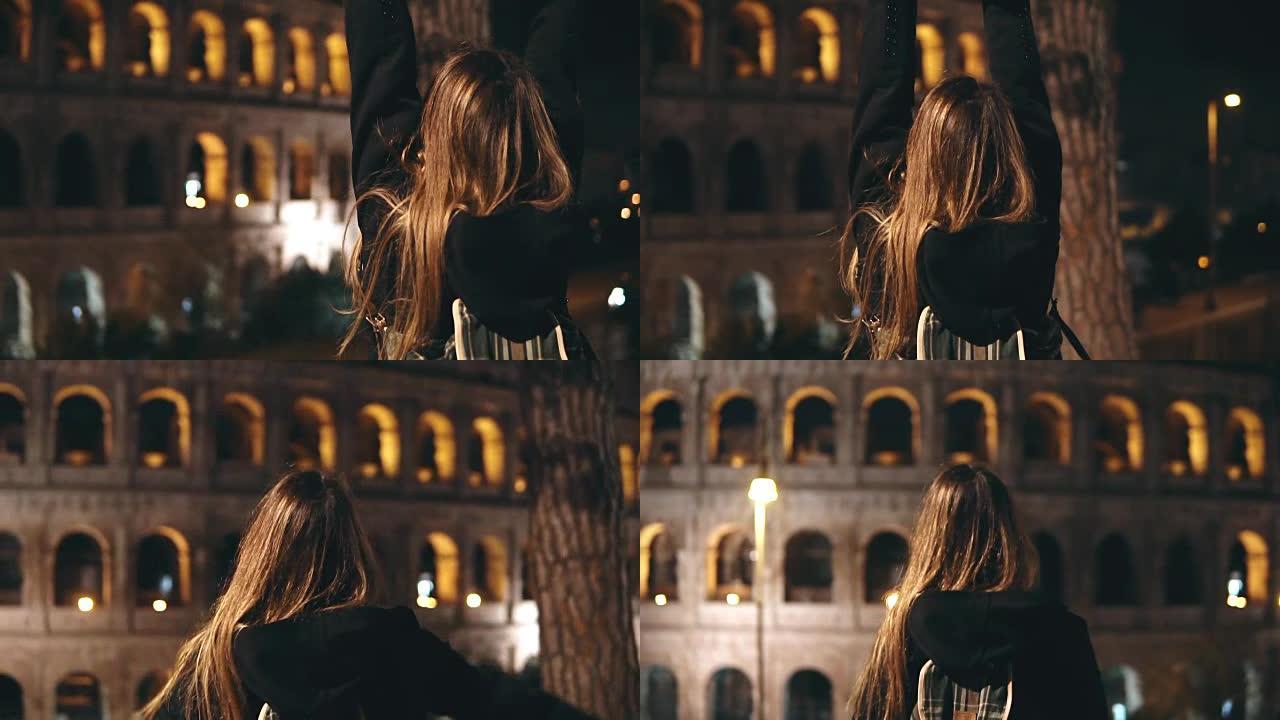 年轻的旅游妇女站在意大利罗马的罗马斗兽场附近，举手看着建筑。慢mo