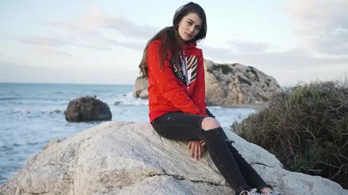 年轻女子在岩石海岸线上摆姿势。日落