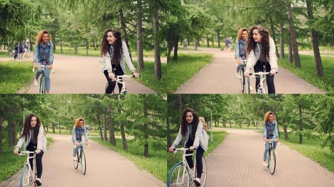多莉拍摄快乐的女学生朋友在公园骑自行车，环顾四周，大笑。美丽的树木和草坪，路过的人是背景。