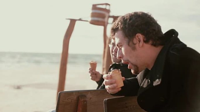 两个年轻人坐在岸边的木凳上吃冰淇淋和说话