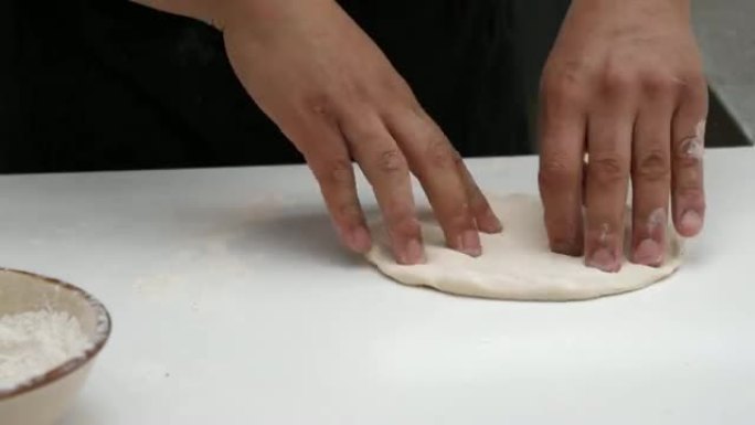 无法辨认的厨师制作比萨饼，揉捏面团并使用金属rolling面杖