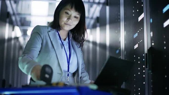 亚洲女性IT工程师工作在一个应急车笔记本电脑，她扫描硬盘。她在满是机架服务器的大数据中心。