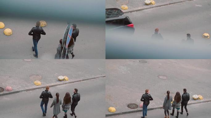 从四个时髦的人走路的街道顶部看。两个女孩和两个男人过马路。慢镜头，稳定镜头