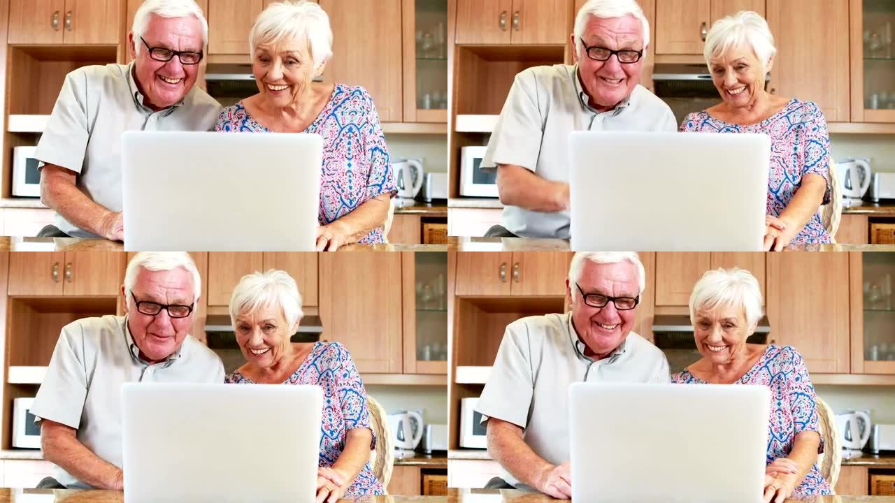 微笑的夫妇在厨房里使用笔记本电脑