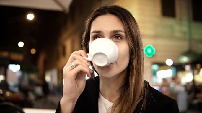 年轻漂亮的女人坐在市中心的咖啡馆，晚上独自一人拿着杯子喝咖啡