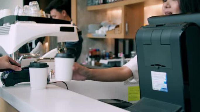 有吸引力的女性员工提供咖啡，并在现代咖啡店从客户那里收取手机NFC付款。