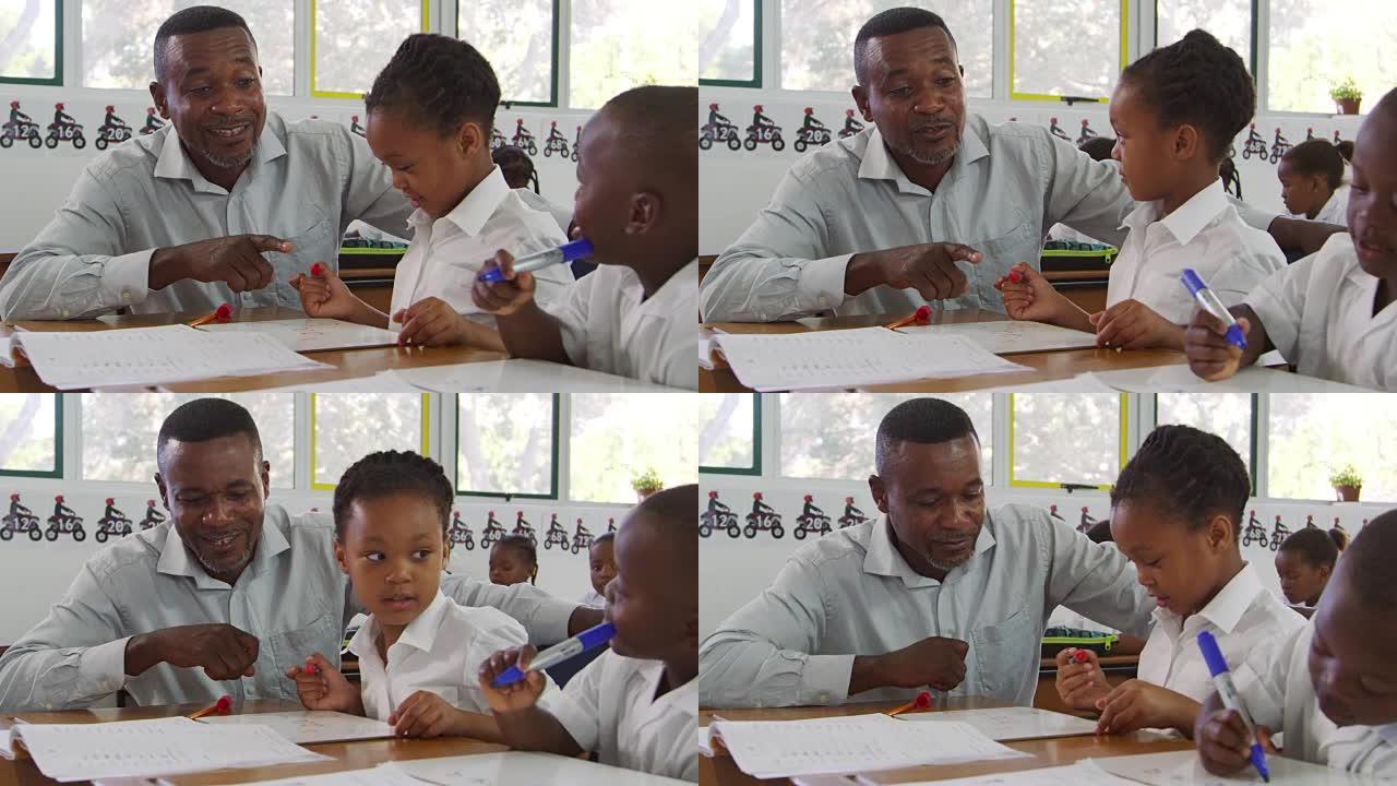 老师在课堂上帮助小学生坐在办公桌前