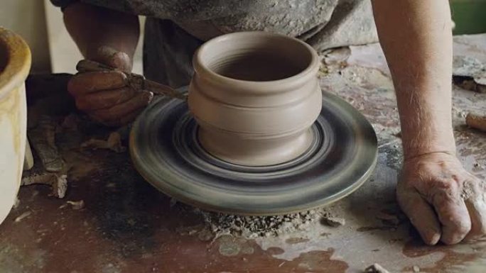 男性双手在旋转陶工的投掷轮上用刀装饰陶瓷锅的特写镜头，制作装饰品。陶器、爱好和手工艺概念。