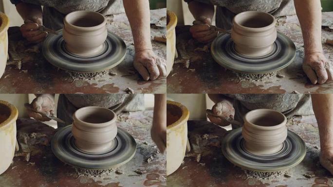 男性双手在旋转陶工的投掷轮上用刀装饰陶瓷锅的特写镜头，制作装饰品。陶器、爱好和手工艺概念。
