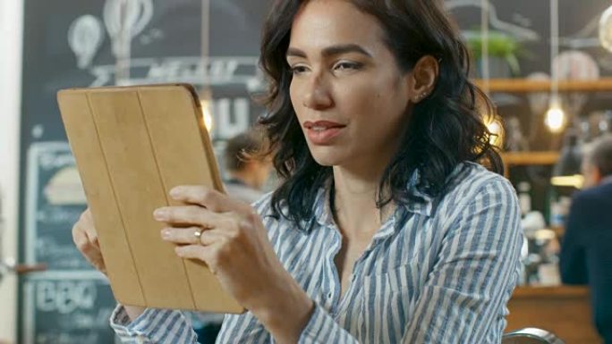 美丽的西班牙裔妇女坐在时尚的咖啡馆里使用平板电脑。