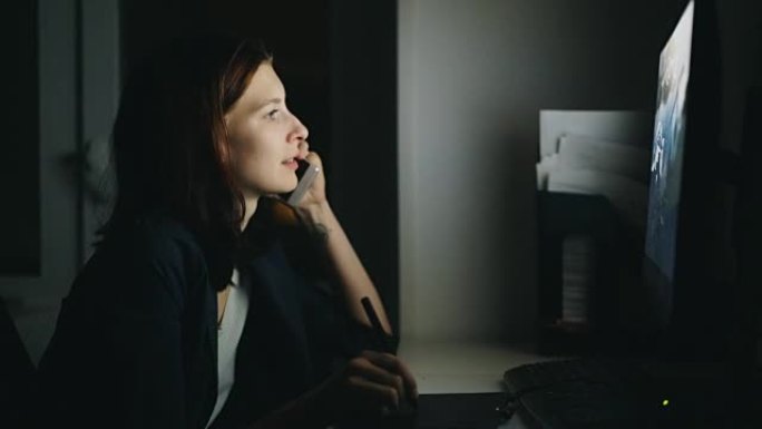 集中的女性设计师通话电话晚上在办公室工作，使用计算机和图形平板电脑完成工作
