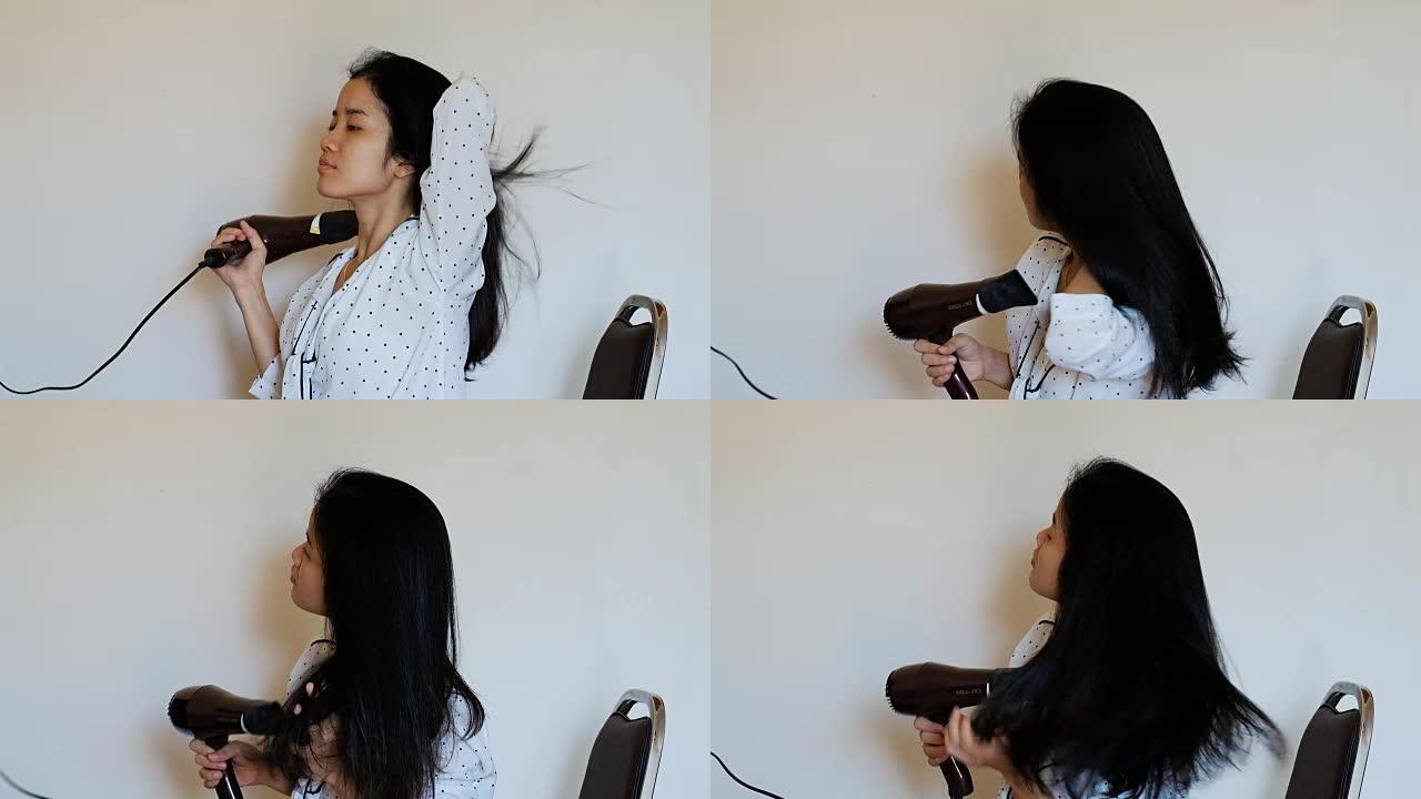 迷人的年轻亚洲女人干吹风机她的长发，坐在卧室的床上。