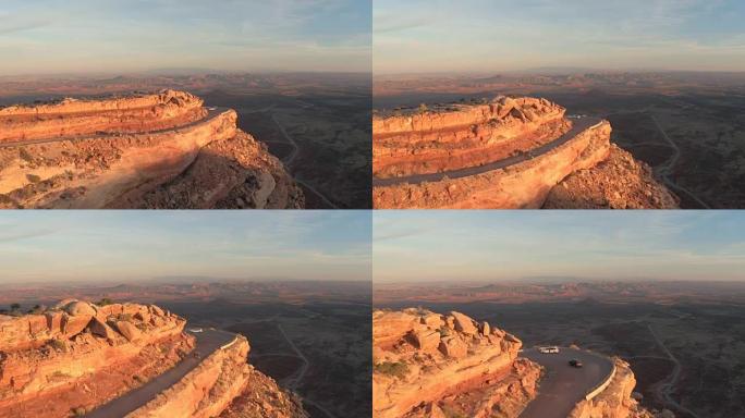 日落时，空中汽车沿着红岩沙漠悬崖在折返路上行驶
