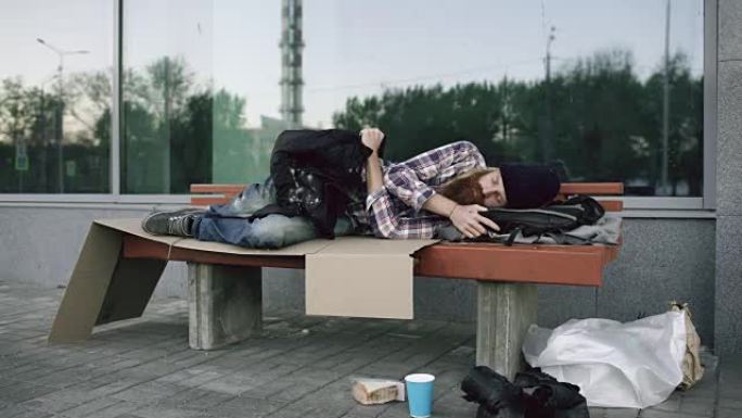 一个无家可归的年轻人试图穿着夹克衫睡在人行道的长椅上